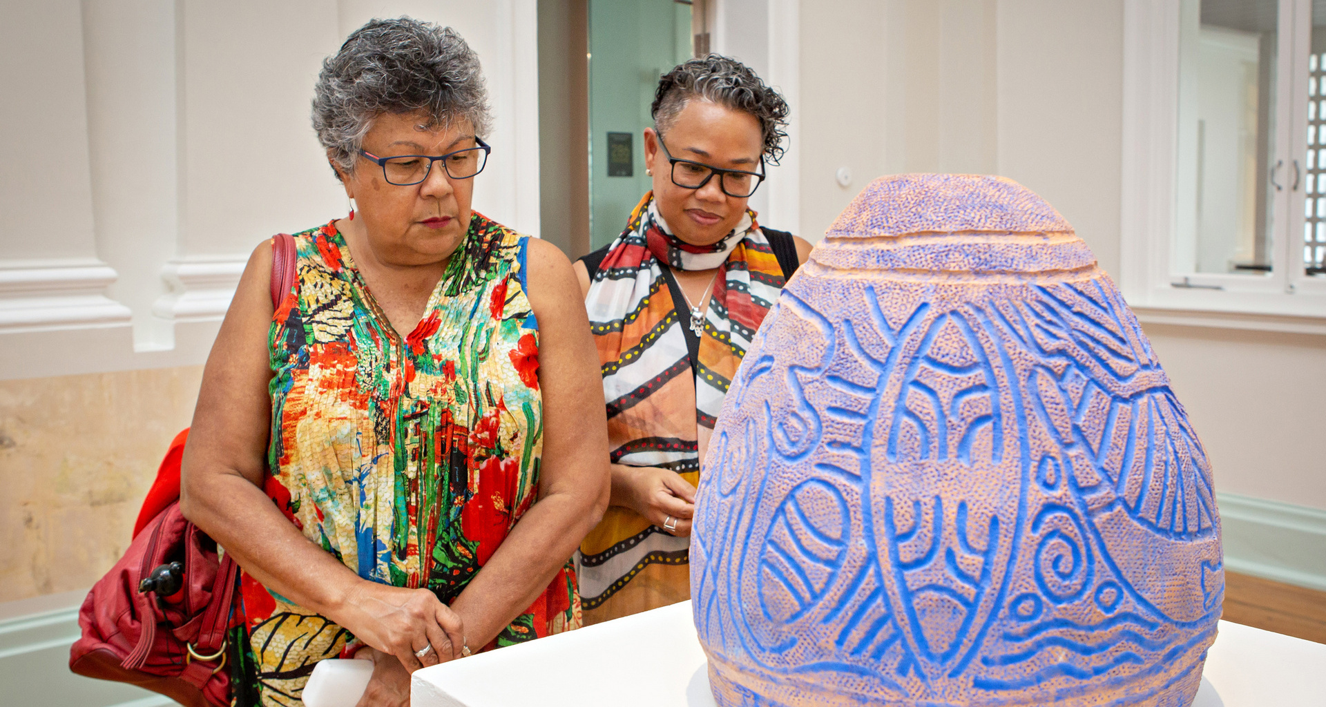 Two women reading information about a ceramic art piece, decorated with traditional patterns