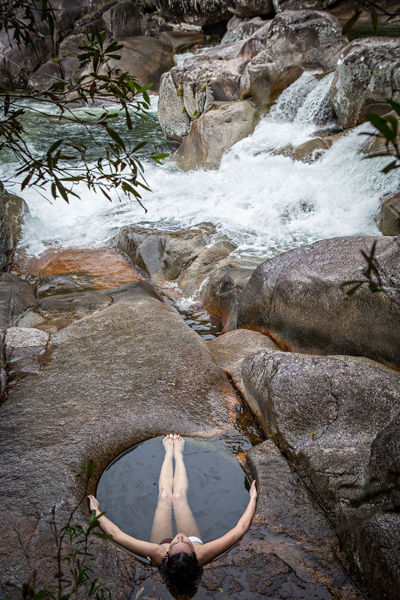 Woman reclining in a rockpool at the edge of a waterfall